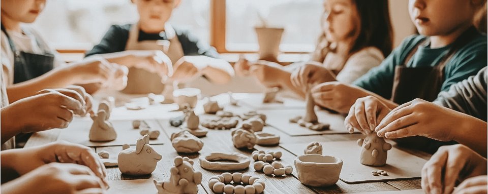 Children sculpting small clay figures at a table at a Painting Prodigies class, hands and clay work in focus