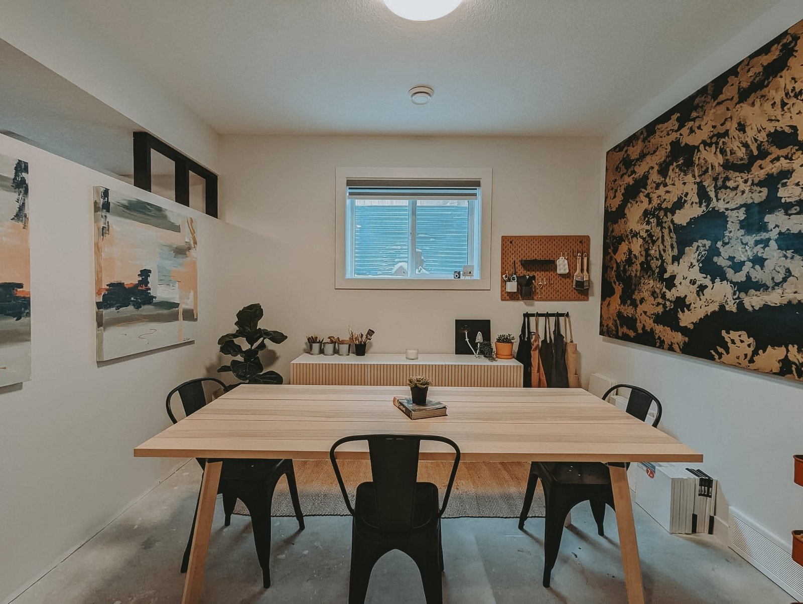 The Painting Prodigies studio in Cochrane: a long wooden table, Leta Taylor's paintings on the walls, and a pegboard of tools