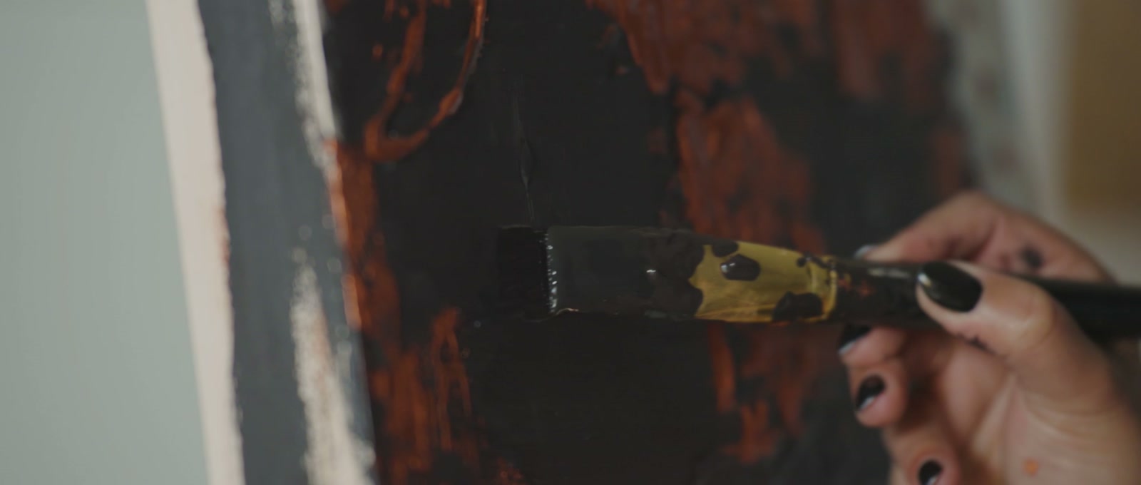 Leta Taylor painting in her Cochrane studio, applying black paint over copper texture with a wide brush